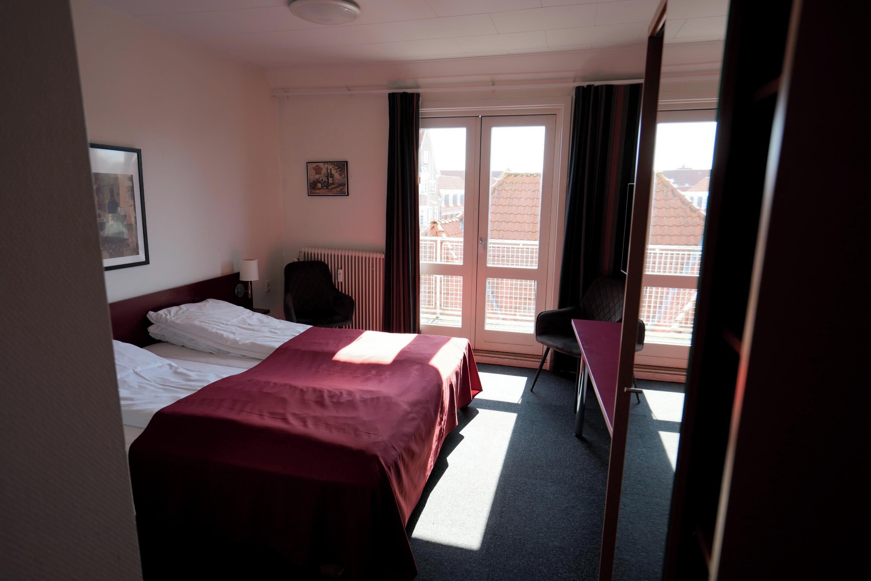 Een hotelkamer met twee bedden, een bureau, een stoel, een radiator en een raam met gordijnen.