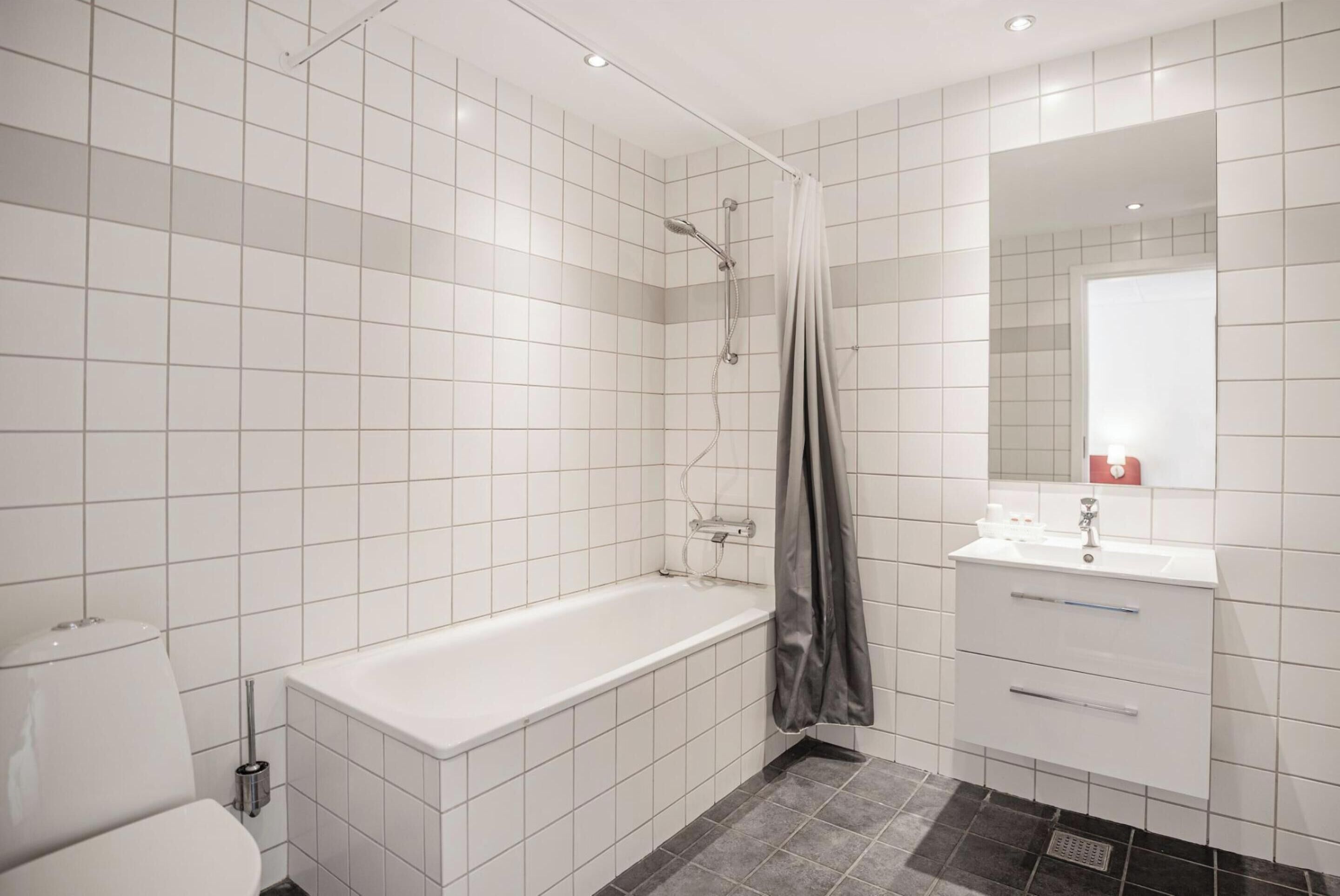 A modern bathroom with white tiled walls, a bathtub, a shower, and a vanity with a mirror.
