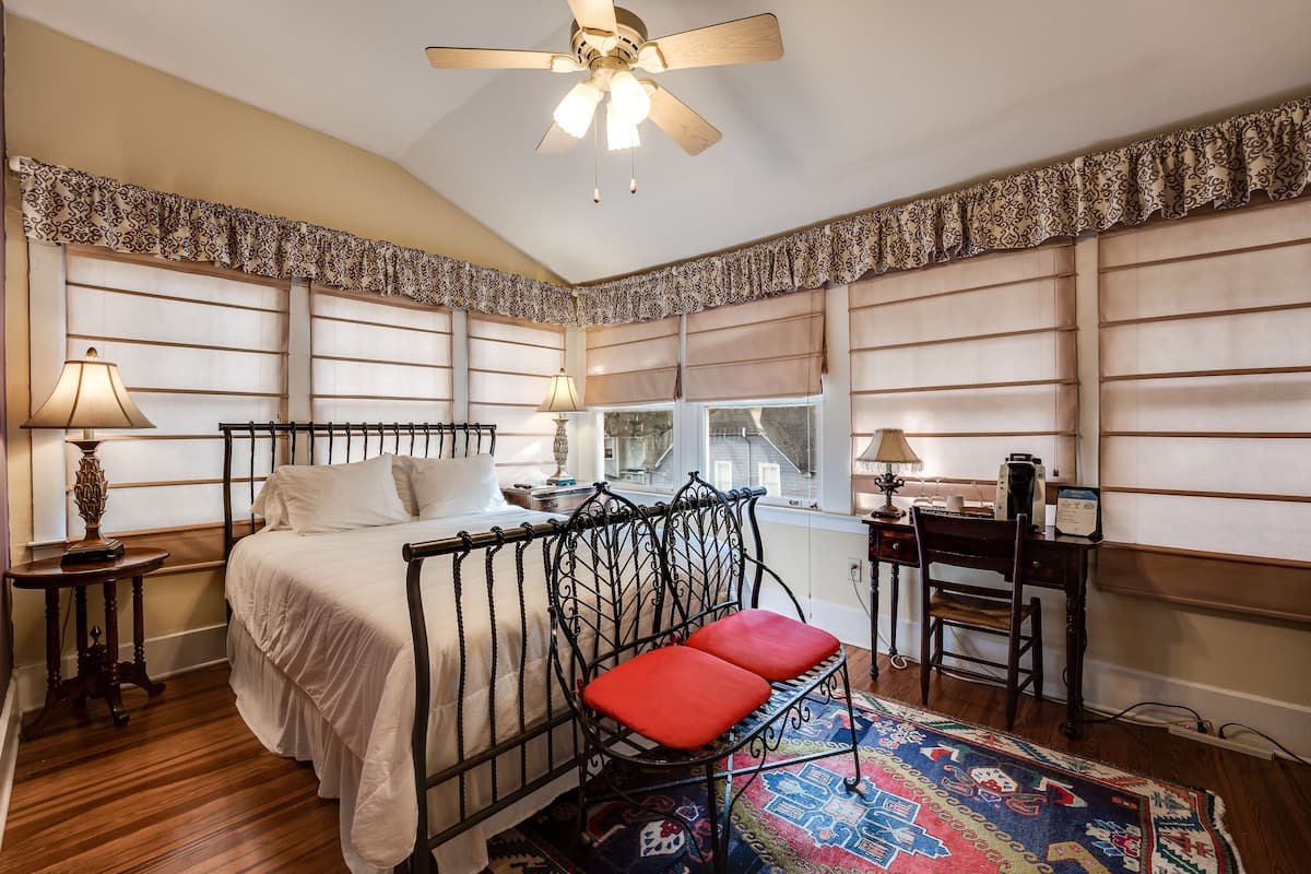 A bedroom with a bed, a chair, a desk, a window, and a ceiling fan.