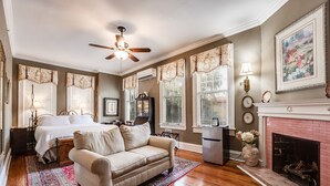 A bedroom with a bed, a sofa, a fireplace, and a ceiling fan. - Riverdale Inn (Jacksonville)