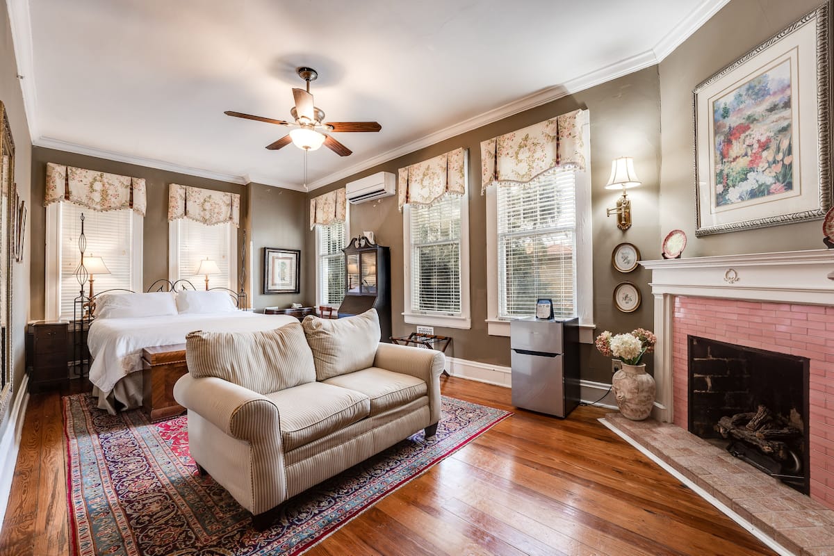 A bedroom with a bed, a sofa, a fireplace, and a ceiling fan.
