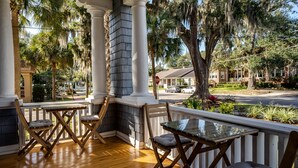 A covered porch with wooden chairs and a glass table, overlooking a street with a house and trees. - Riverdale Inn (Jacksonville)