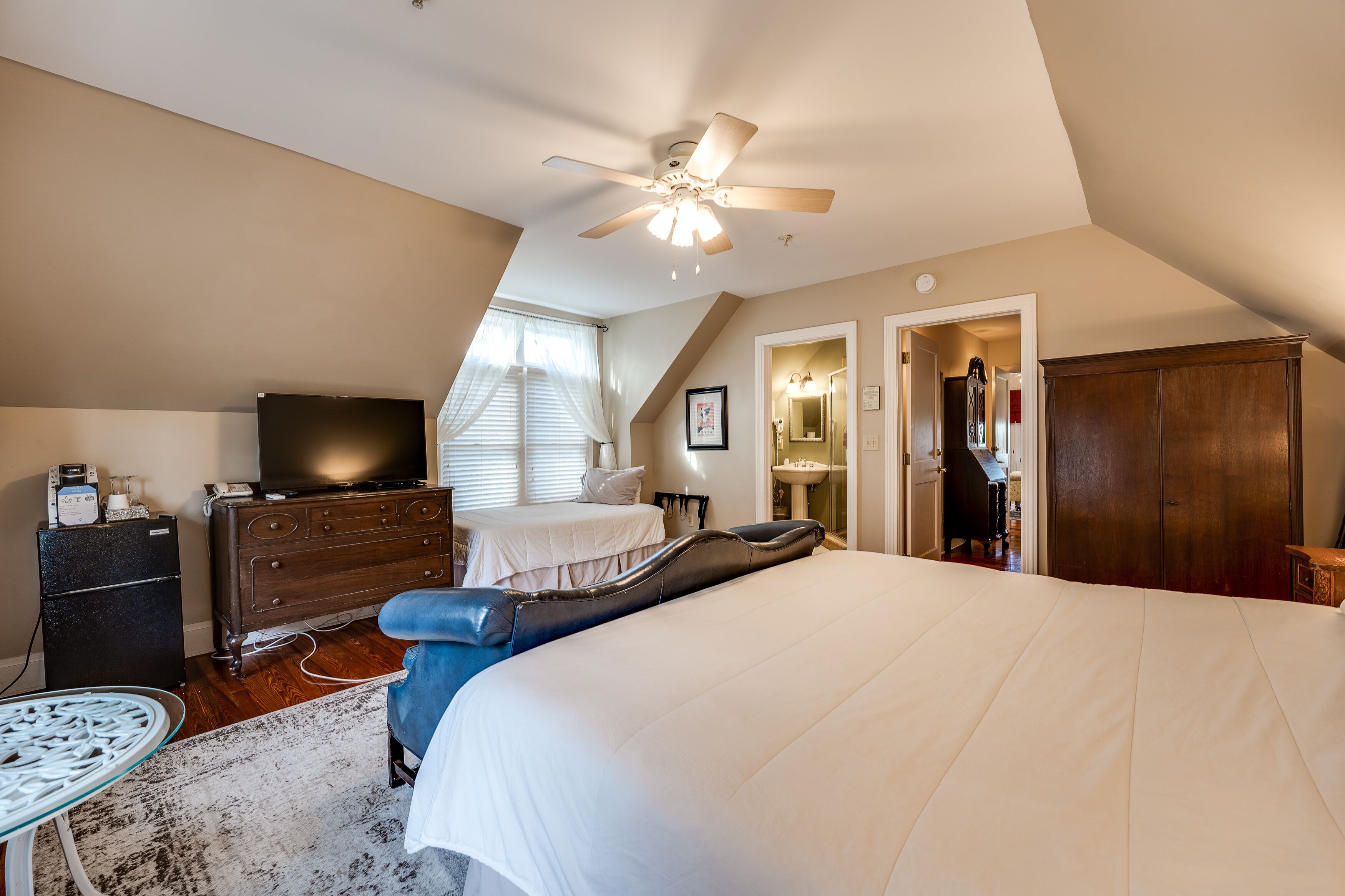 A bedroom with a large bed, a ceiling fan, a dresser, a television, and a desk with a chair.
