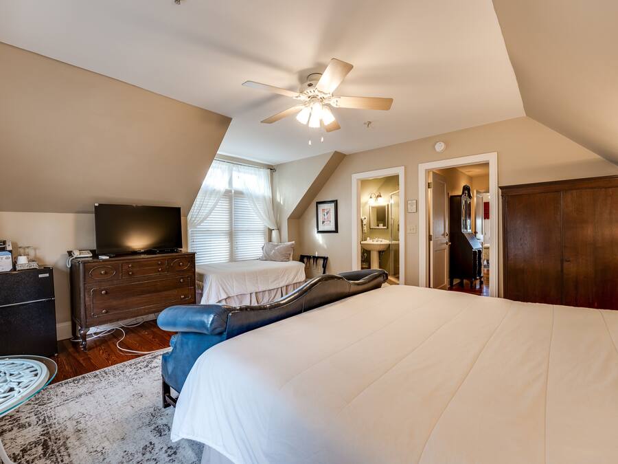 A bedroom with a large bed, a ceiling fan, a dresser, a television, and a desk with a chair.