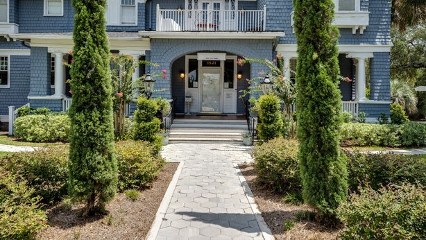 A large, two-story house with a covered front porch, a balcony, and a well-maintained garden with trimmed bushes and a stone pathway leading to the entrance. - Riverdale Inn (Jacksonville)