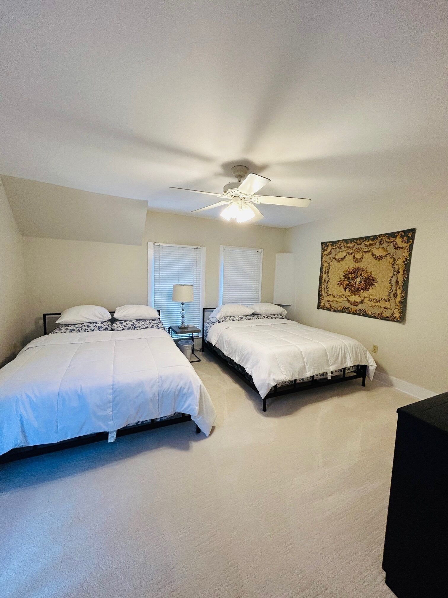 A bedroom with two beds, a ceiling fan, and a large tapestry on the wall.