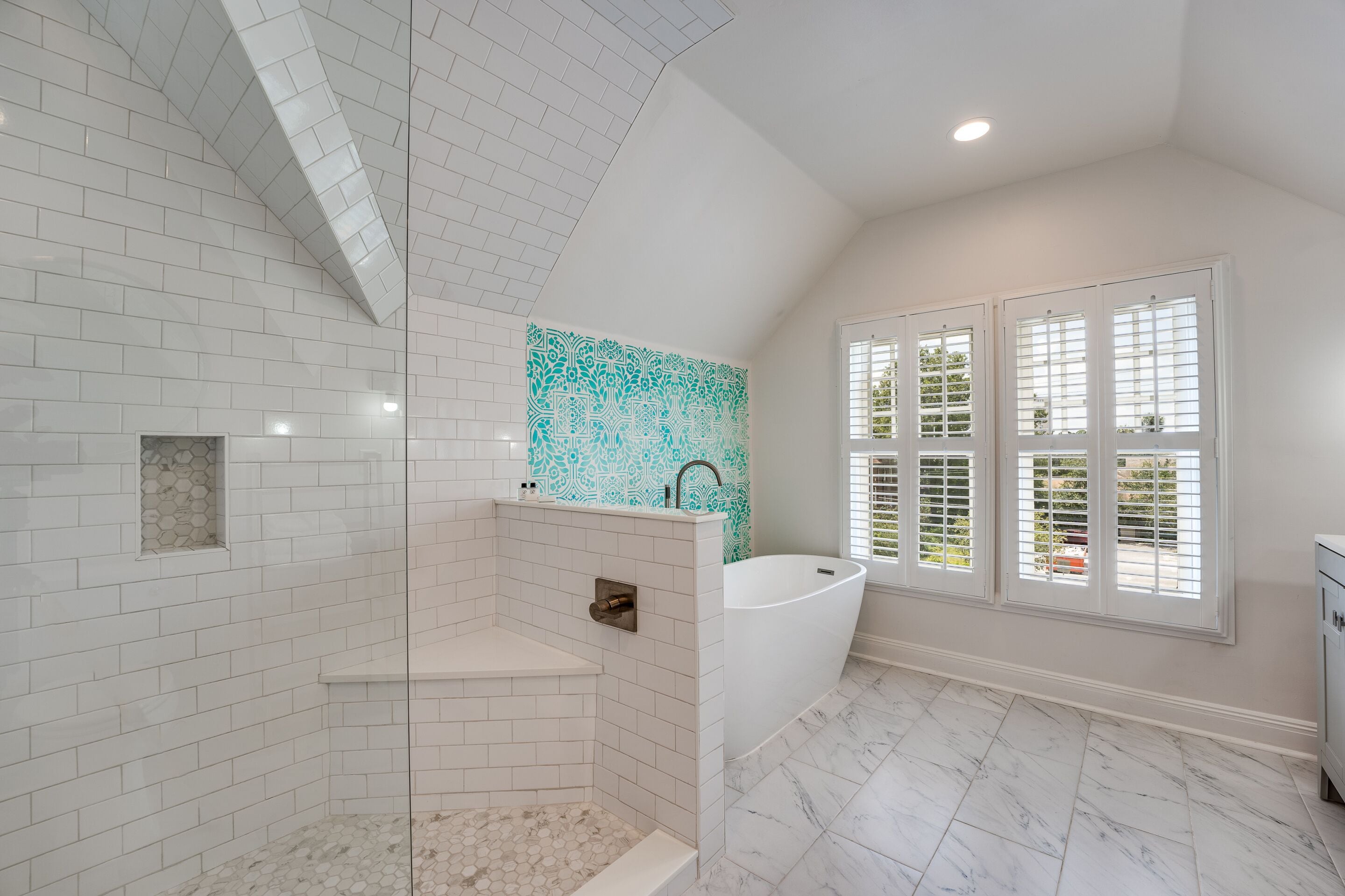 A modern bathroom with white subway tiles, a freestanding bathtub, a shower area, and a window with blinds.