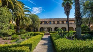 A courtyard with a central pathway, surrounded by neatly trimmed hedges and palm trees.