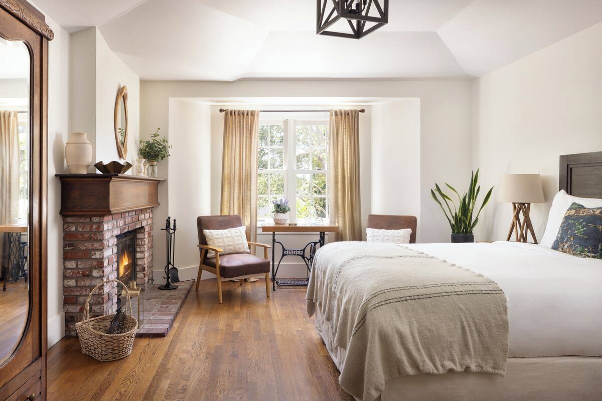 Un dormitorio con chimenea de ladrillo, un escritorio de madera, una cama y una ventana con cortinas.