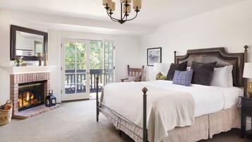 A bedroom with a large bed, a fireplace, a chandelier, and a view through a glass door.