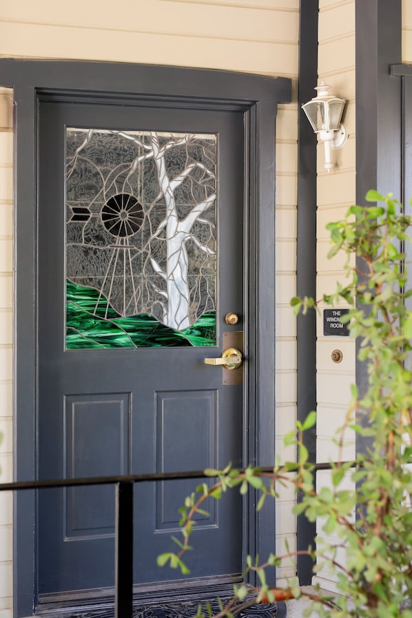 A dark blue door with a glass panel featuring a tree and a windmill design.