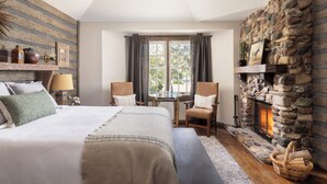 A bedroom with a large bed, a stone fireplace, and a window with curtains.
