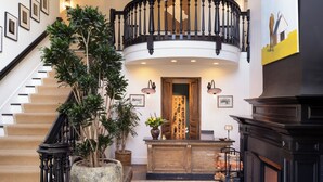 A grand foyer with a staircase, chandelier, and a large potted plant.