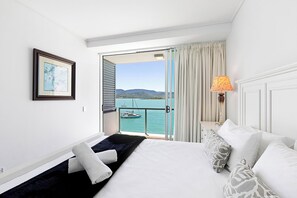 A hotel room with a bed, a nightstand, a lamp, a framed picture, and a view of the sea and boats through an open door. - Peninsula Airlie Beach (Airlie Beach)