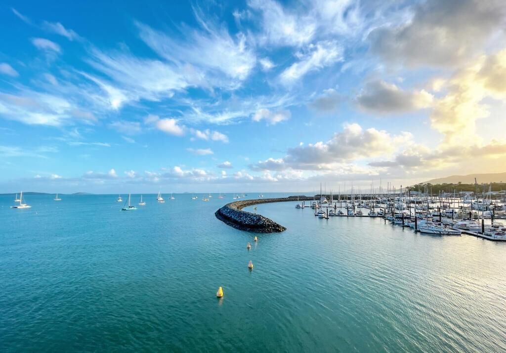 A marina with boats docked, a breakwater, and a clear sky.