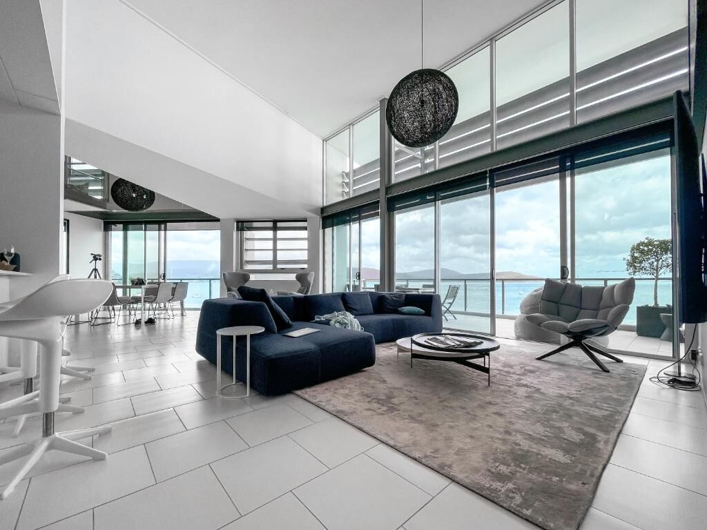 A modern living room with a large sofa, a coffee table, and a view of the ocean through large windows.