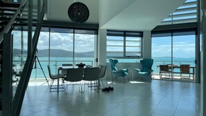 Een ruime woonkamer met uitzicht op zee, een trap en modern meubilair.