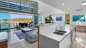 Een moderne keuken met een groot eiland, een eethoek met uitzicht op de jachthaven, en een woonruimte met een bank en salontafel.