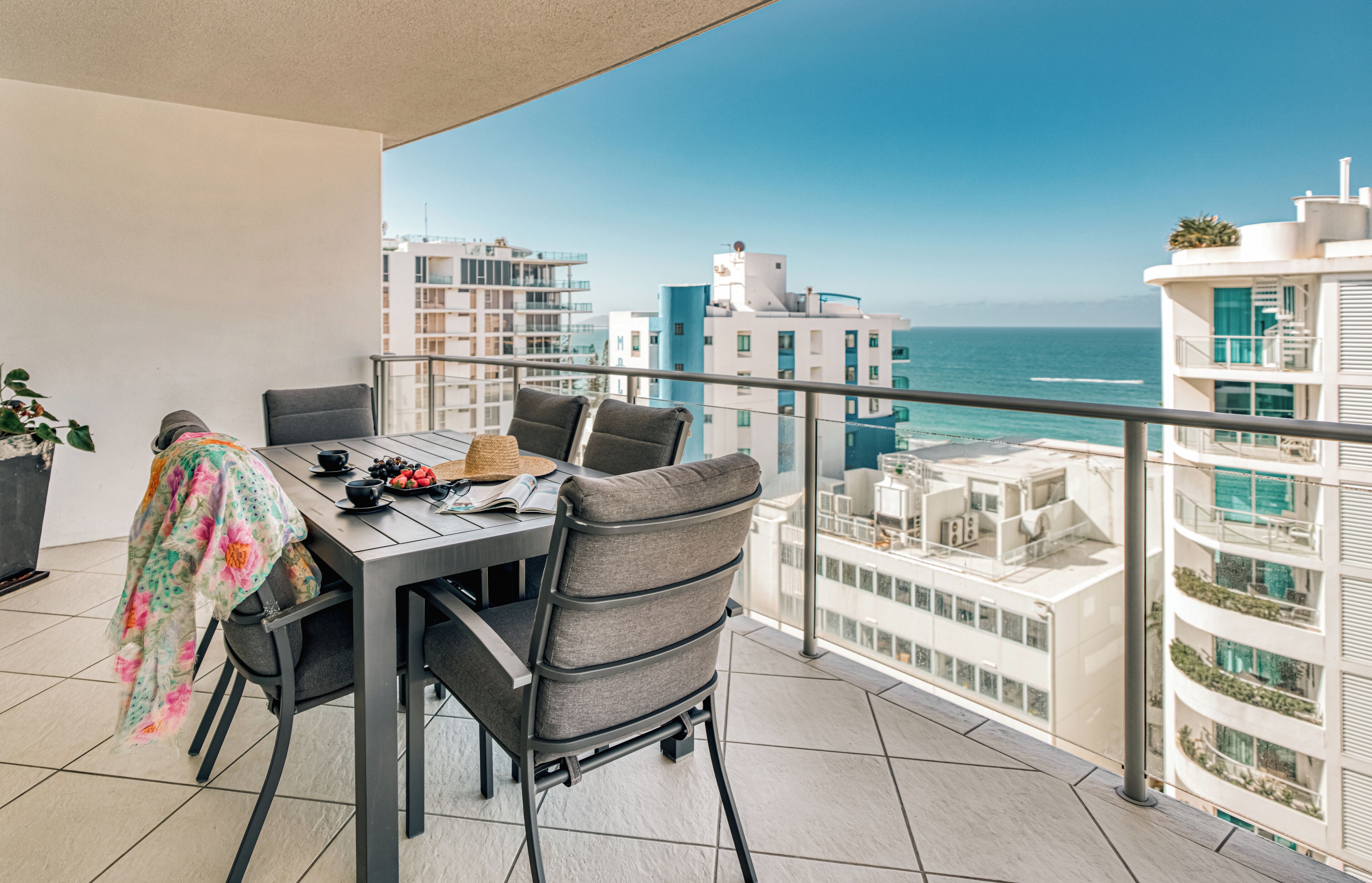 A balcony with a dining table, chairs, and a view of the ocean and buildings.