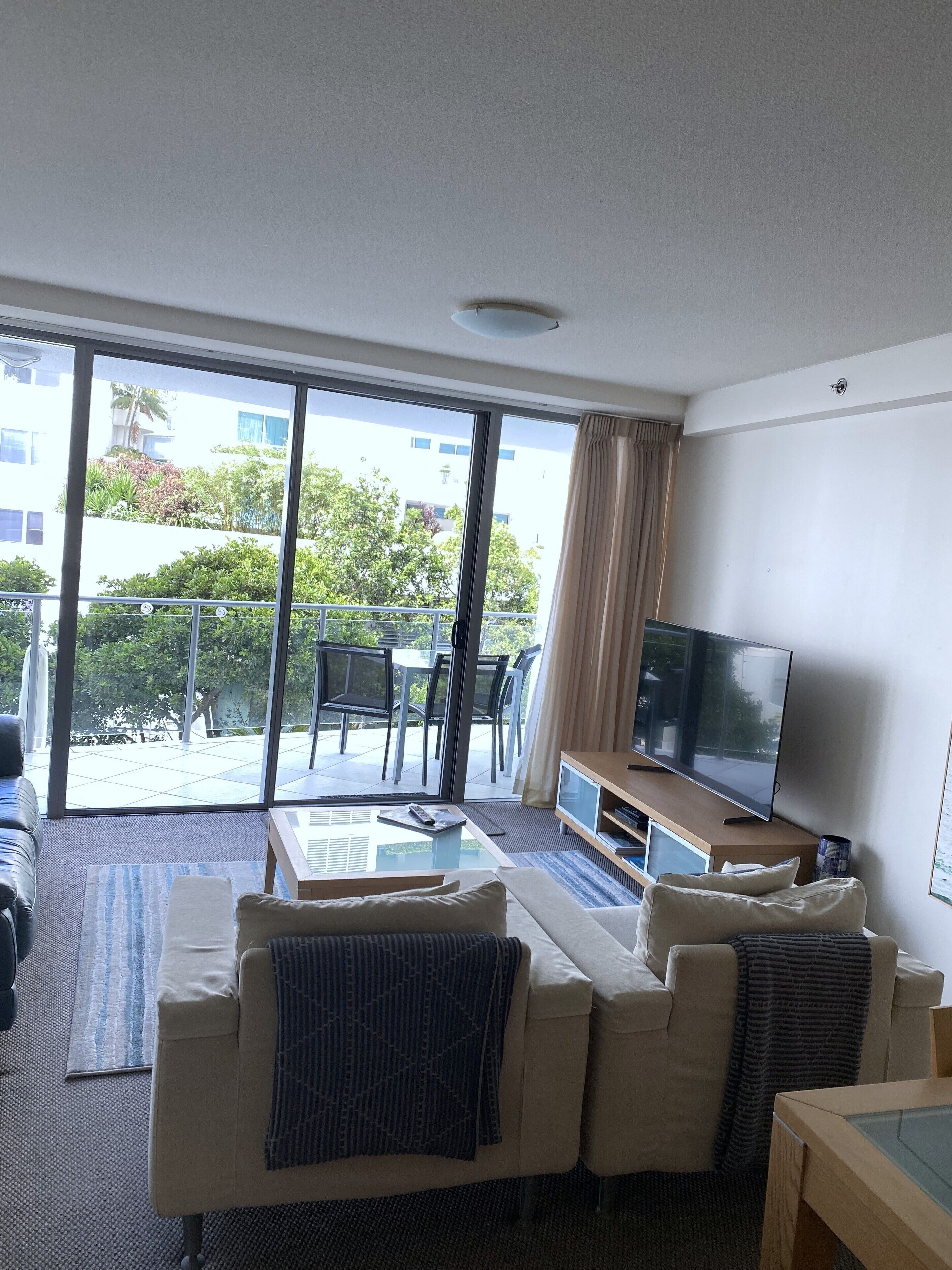 A modern living room with a sofa, TV, and a balcony with outdoor furniture.