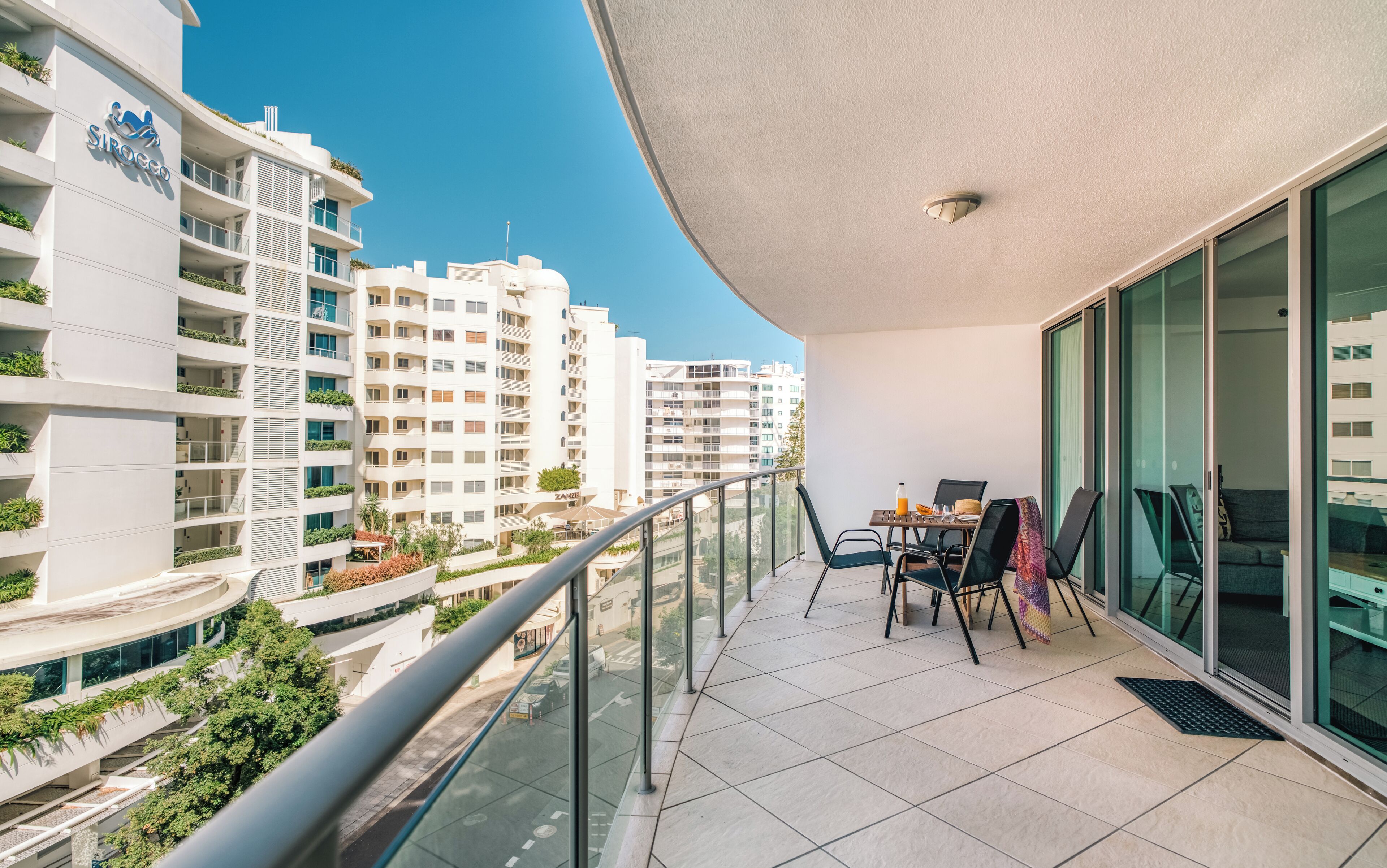 A balcony with a table and chairs, overlooking a cityscape with modern buildings.