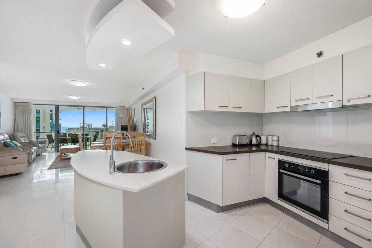 A modern kitchen with white cabinets, a central island with a sink, and a built-in oven.