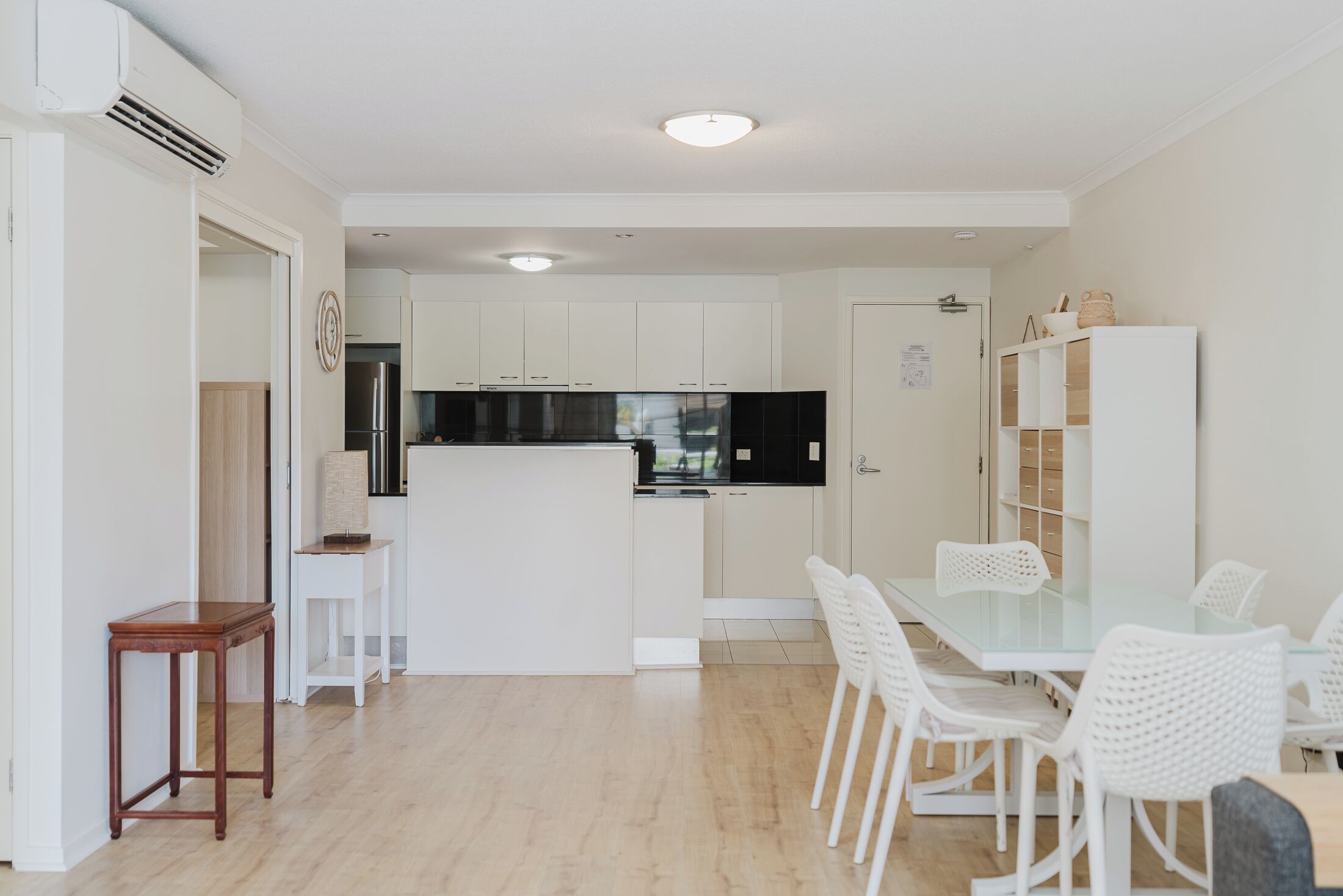 A modern kitchen with white cabinets, a central island, and a dining area with white chairs.