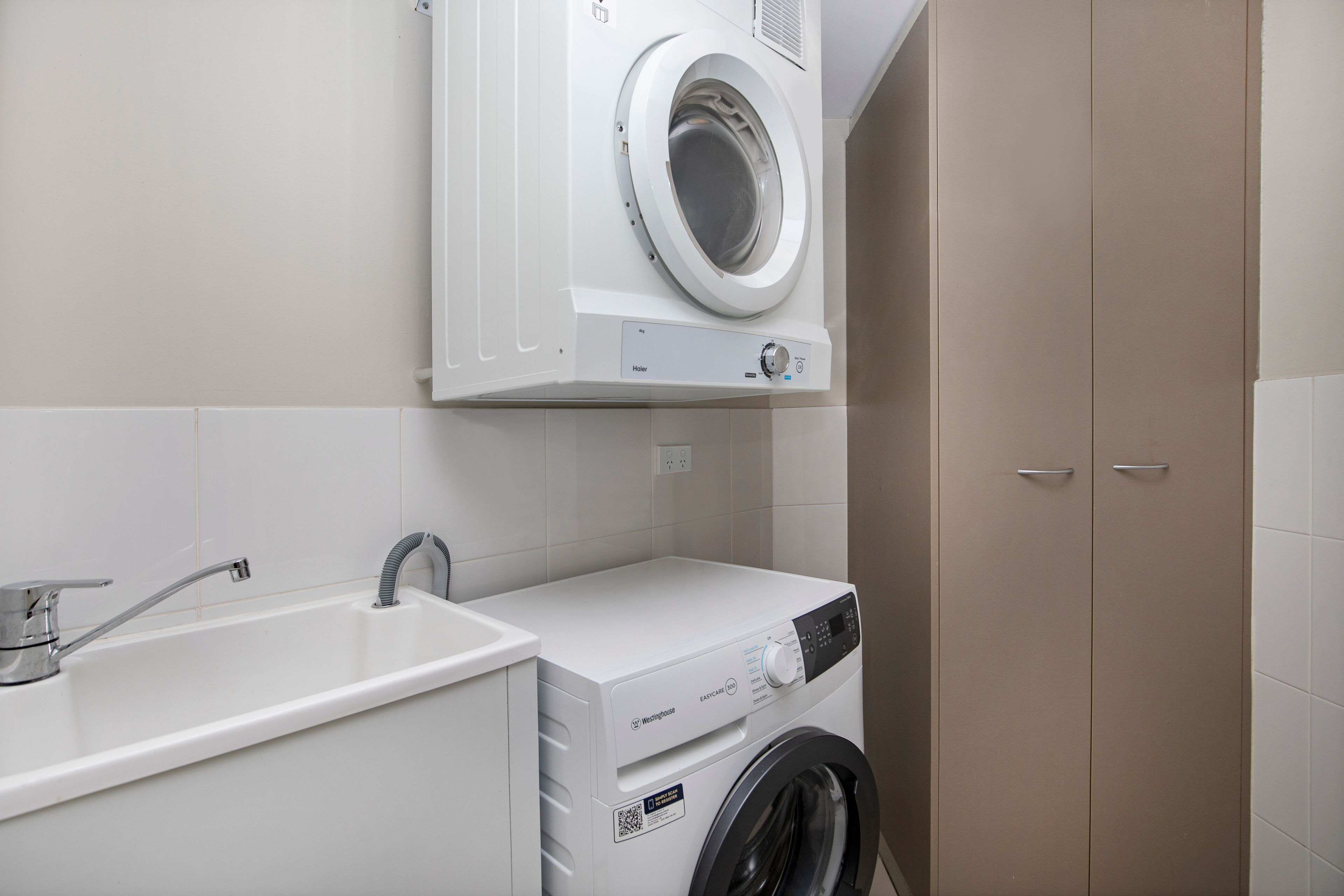 Een kleine wasruimte met een wasmachine, een wasbak en een kast.