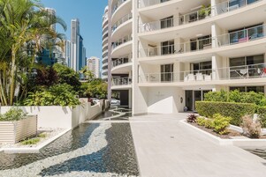 Un hotel moderno de varios pisos con un patio central que incluye una fuente y zonas ajardinadas.