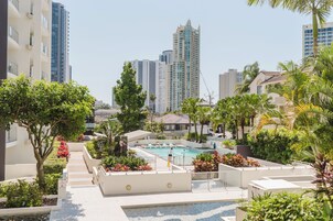 Zona de piscina en la azotea con vistas a rascacielos, rodeada de vegetación y palmeras.