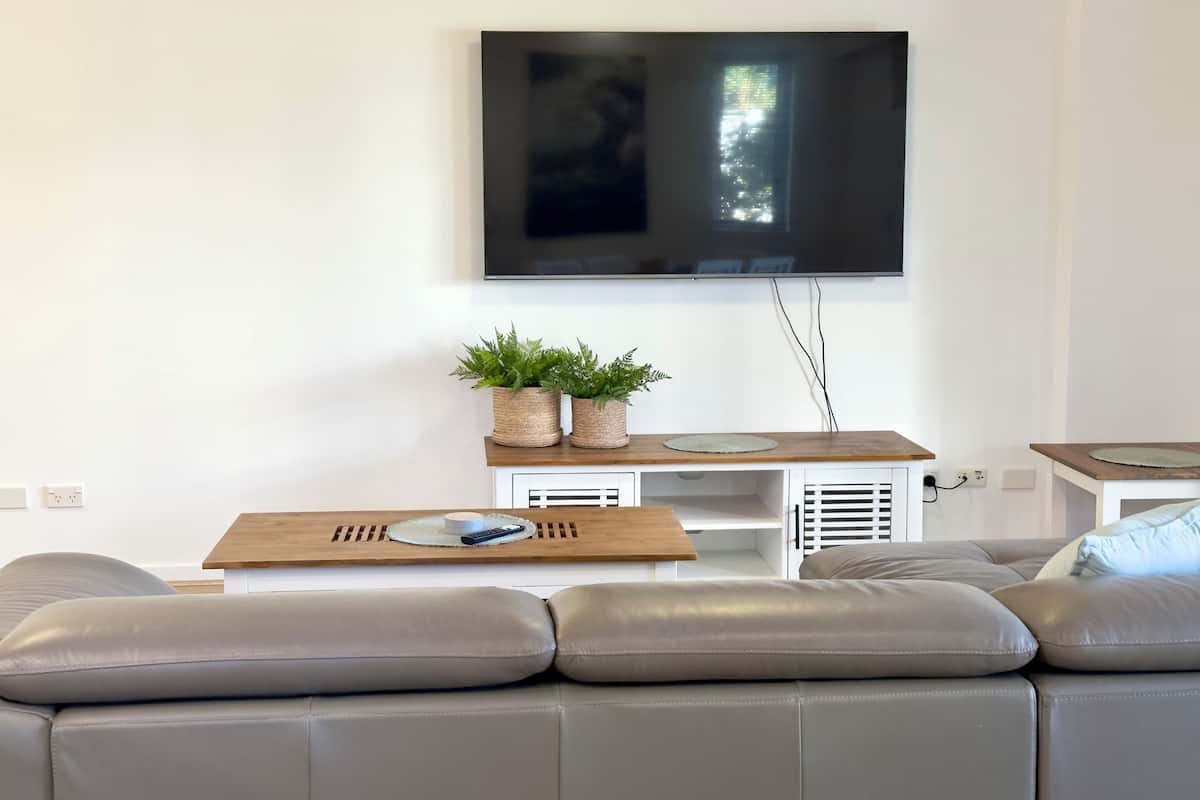 A modern living room with a leather sofa, a wooden coffee table, and a flat-screen TV mounted on the wall.