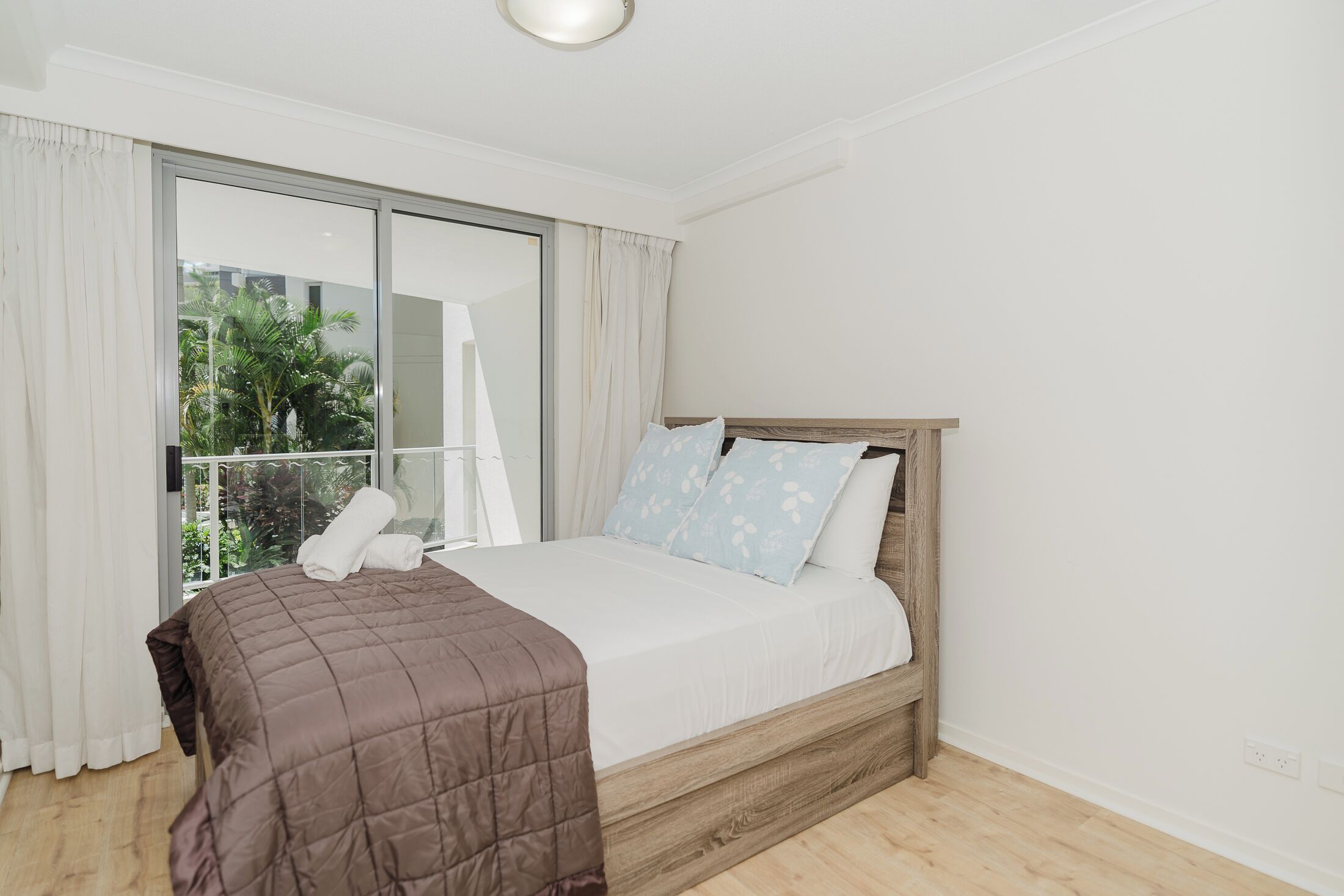 Un dormitorio con cama, ventana con cortinas y vistas al verdor exterior.