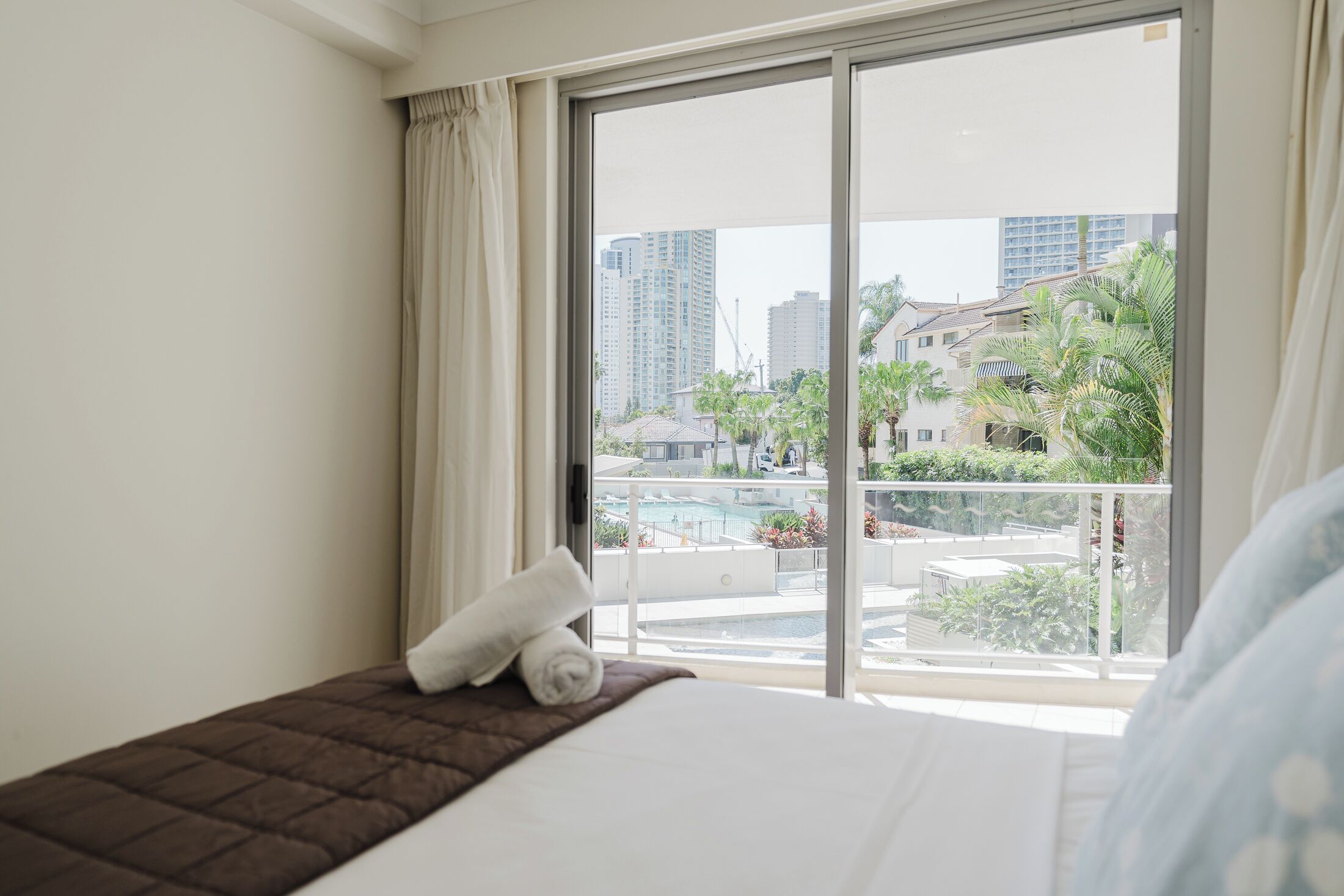 A hotel room with a large window, a bed, and a view of a swimming pool and buildings.