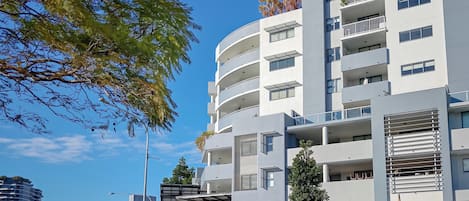 Un immeuble à plusieurs étages dont le rez-de-chaussée est affecté à des commerces, notamment une boutique et une terrasse extérieure.