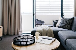 Una sala de estar moderna con una mesa de centro redonda de madera, una cesta trenzada negra, una taza blanca y una revista.