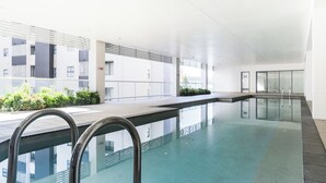 Una piscina coberta moderna amb parets de vidre transparent, una escala metàl·lica i un disseny net i minimalista.