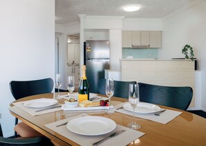 Una mesa de comedor dispuesta con platos, cubiertos, copas, una botella de champán y un cuenco pequeño de aceitunas.
