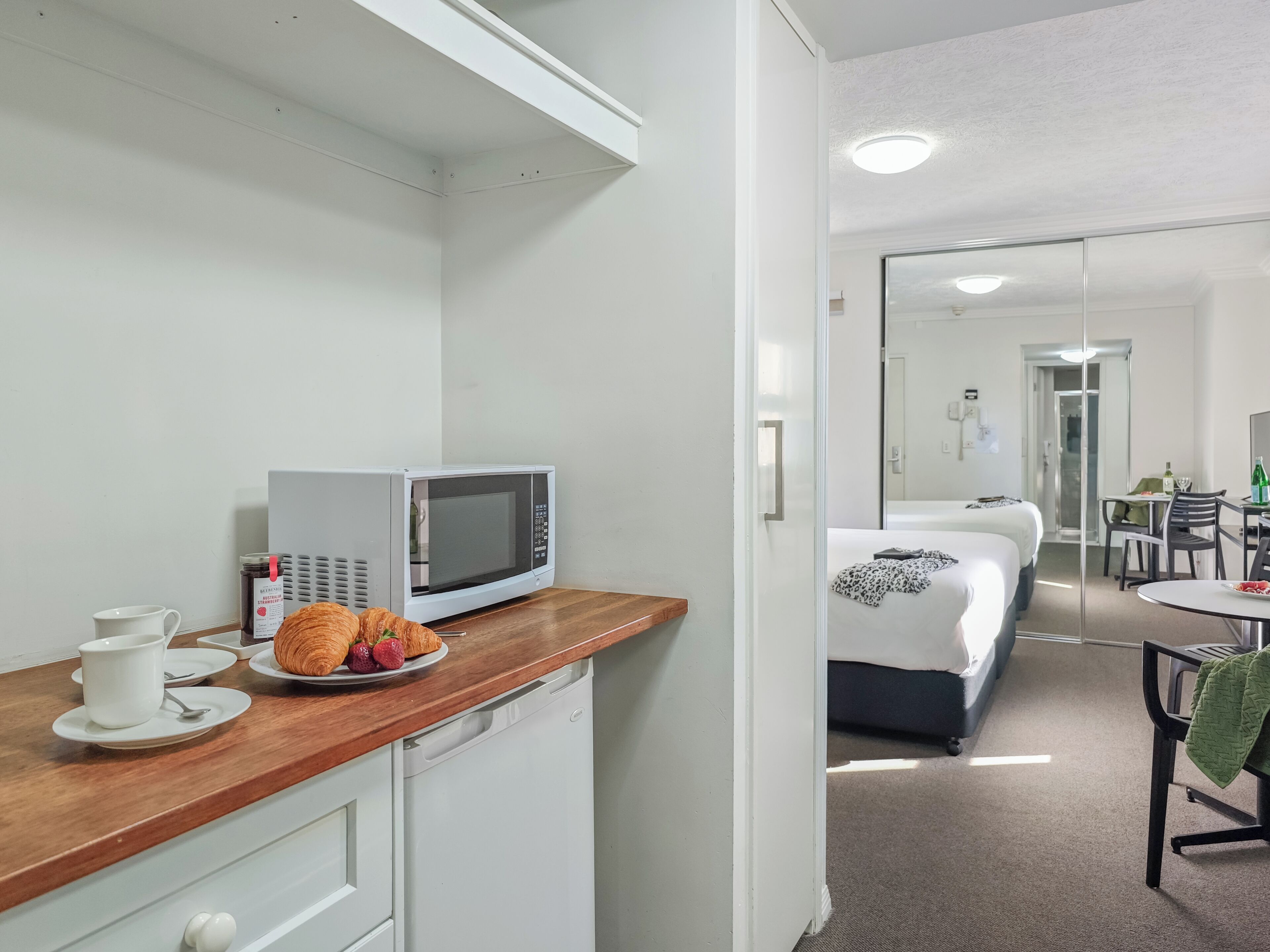 A kitchenette with a microwave, a coffee maker, and croissants on the counter.
