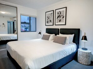 A hotel room with a large bed, two bedside tables, a mirror, and artwork on the wall. - Gabba Central Apartments (Woolloongabba)