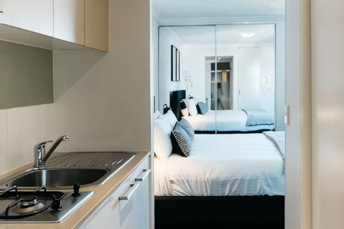 Habitación de hotel moderna con kitchenette, cama con ropa blanca y vista del interior de la habitación.