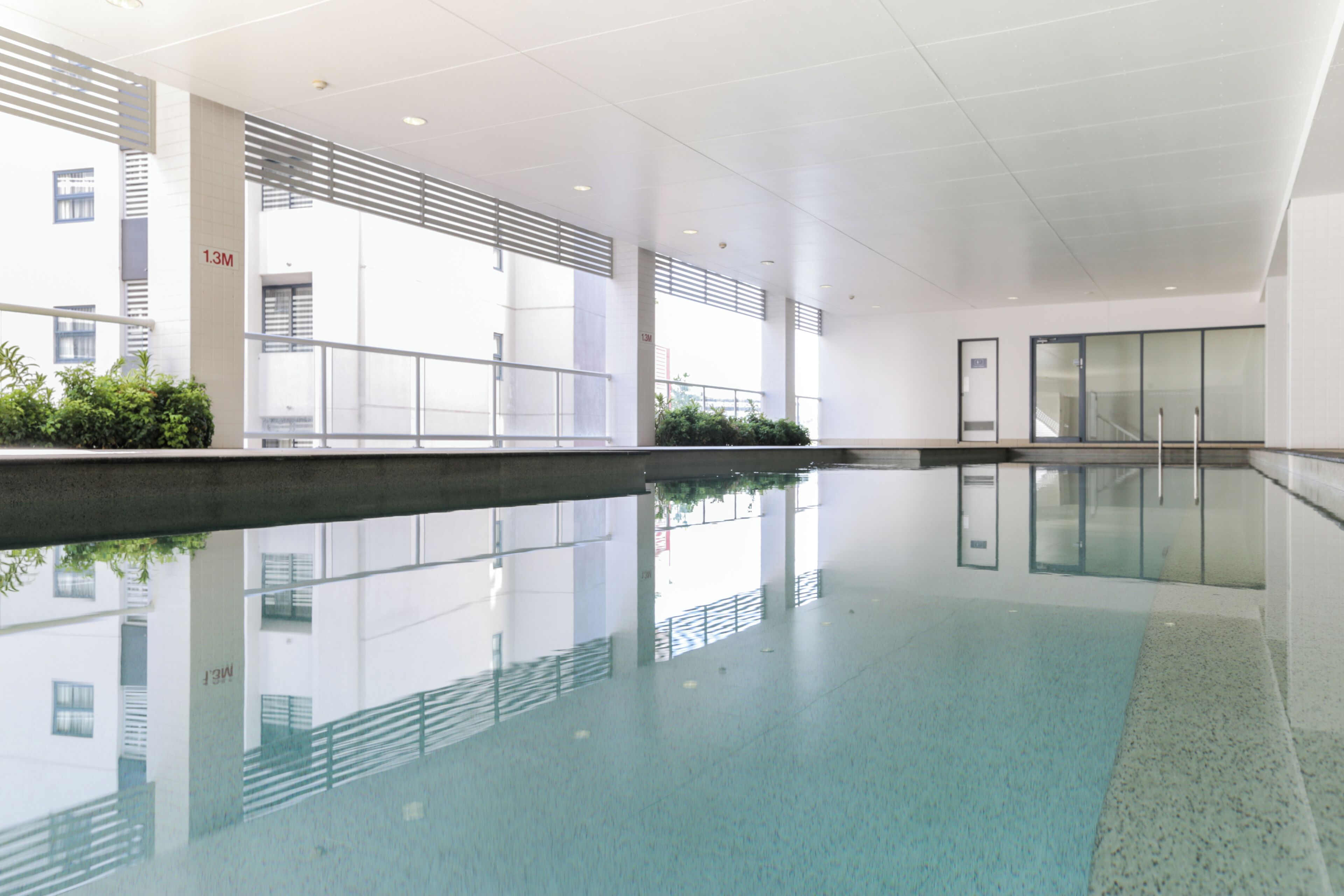 A modern indoor swimming pool with clear water, surrounded by a spacious area with a high ceiling and large windows.