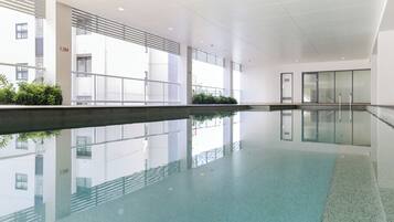 A modern indoor swimming pool with clear water, surrounded by a spacious area with a high ceiling and large windows.