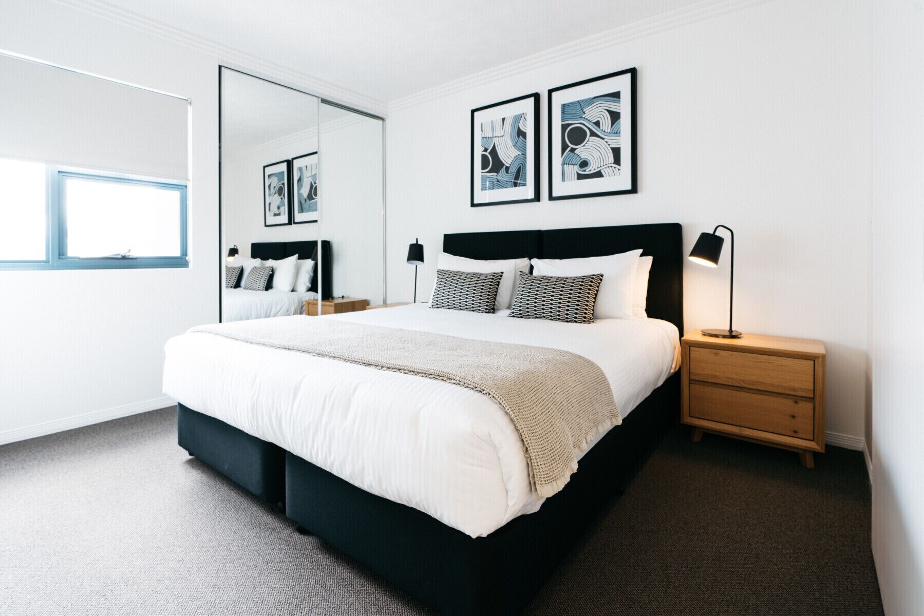 A modern bedroom with a large bed, bedside tables, a mirror, and framed artwork on the wall.