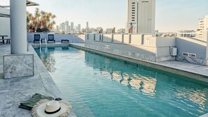 A rooftop pool with clear blue water, a lounge area with chairs, and a city skyline in the background. - Gabba Central Apartments (Woolloongabba)