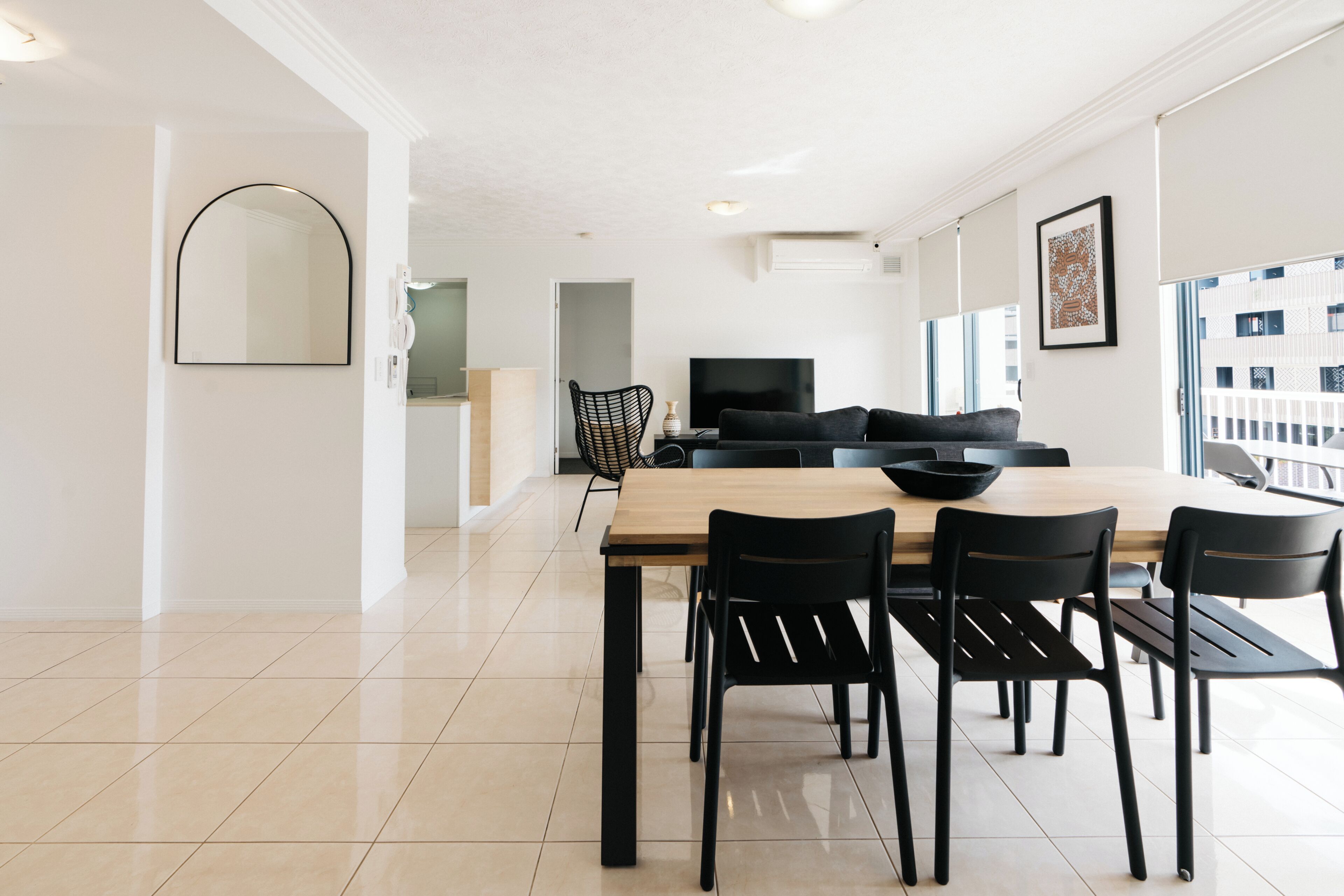A modern dining area with a wooden table and black chairs, a black sofa, and a large window with a view of buildings.