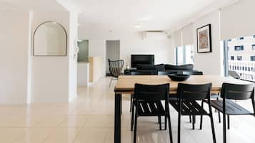 A modern dining area with a wooden table and black chairs, a black sofa, and a large window with a view of buildings.