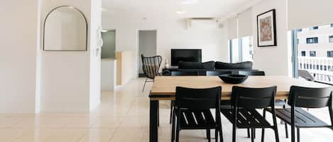 A modern dining area with a wooden table and black chairs, a black sofa, and a large window with a view of buildings.