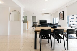 A modern dining area with a wooden table and black chairs, a black sofa, and a large window with a view of buildings.