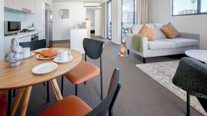 A modern hotel room with a dining area, kitchenette, and a sofa with cushions. - Gabba Central Apartments (Woolloongabba)