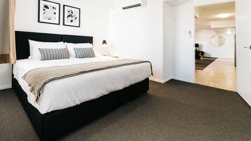 A hotel room with a large bed, a headboard, two bedside tables with lamps, a carpeted floor, and a door leading to a hallway.